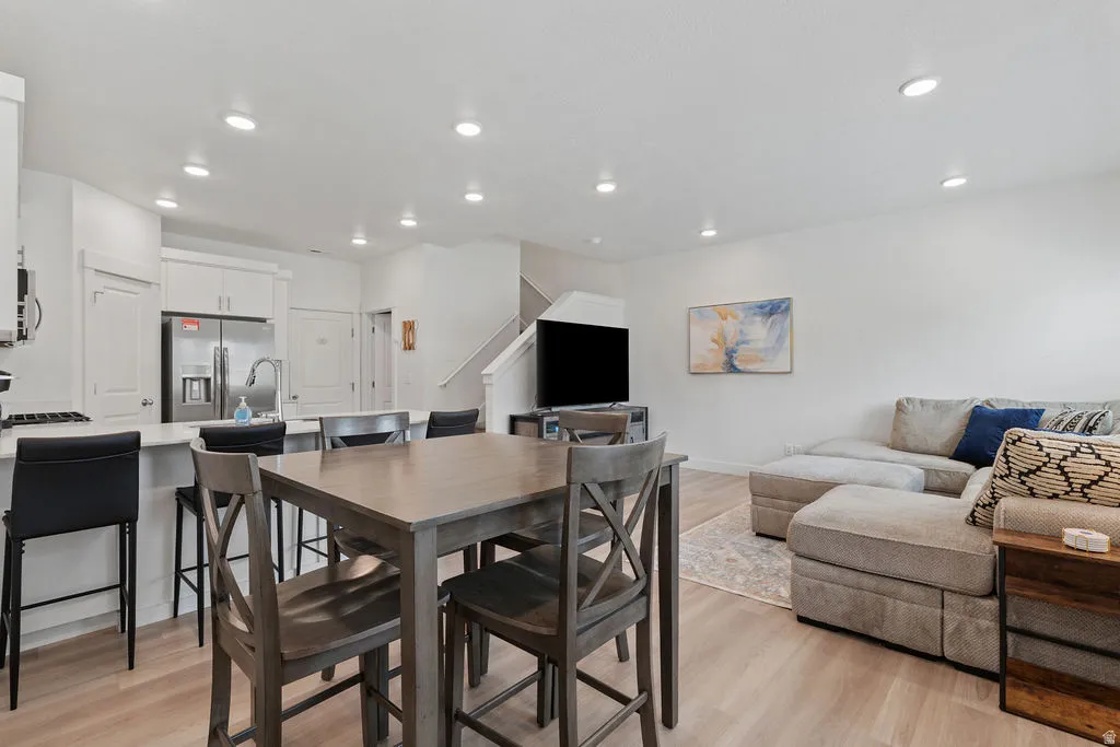 Open-concept living space featuring wood-finish flooring throughout, a kitchen island with seating, recessed lighting, and a white staircase