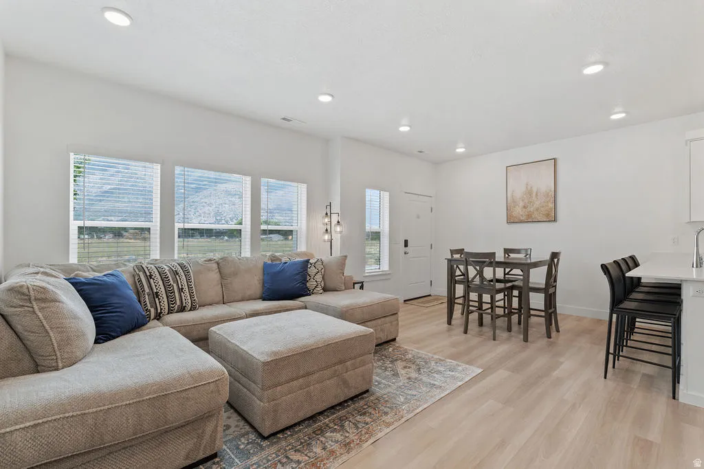 Bright open-concept living area featuring light wood-finish flooring, recessed lighting, and white walls