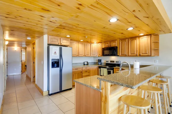 Kitchen featuring wood-finish cabinetry, granite-style countertops, stainless steel refrigerator, and recessed ceiling lighting