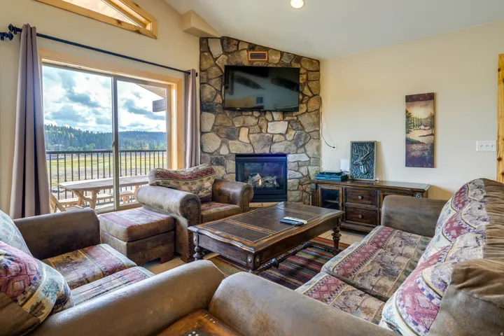 Living area with a floor-to-ceiling stone fireplace, a wall-mounted television, and a wood-finish media console