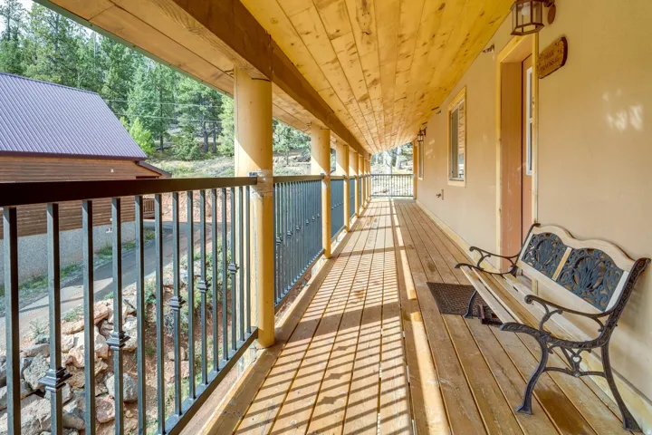 Expansive covered wooden deck featuring natural wood flooring, exposed wood beam ceiling, round support columns, and decorative metal railings