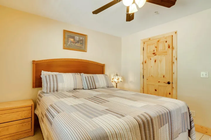 Spacious room featuring a wood headboard, paneled wood door, wood-finish ceiling fan with integrated lighting, and neutral wall tones