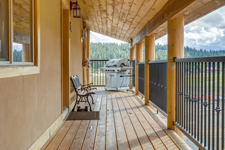 Expansive wood-finish deck with log columns, horizontal wood-plank ceiling, and black metal railings