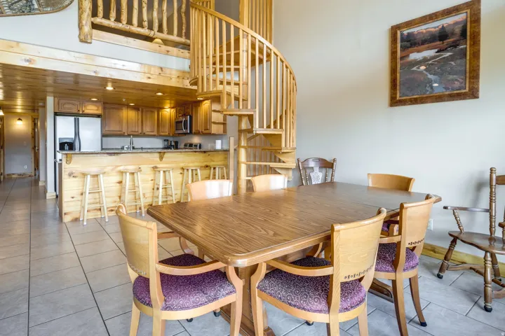 Open-concept dining area featuring a wood-finish table, adjacent kitchen with wood cabinetry and stainless steel appliances, and a prominent wood spiral staircase