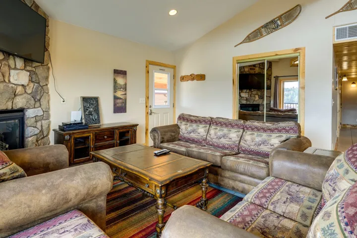 Living room featuring a stone fireplace with a black insert, vaulted ceilings, light-toned walls, and wood-trim accents