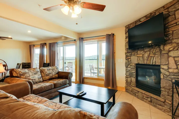 Spacious living area featuring a floor-to-ceiling stone fireplace, light tile flooring, and multiple sliding glass doors leading to an exterior balcony