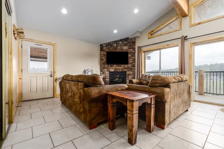 Stone-faced fireplace with hearth, ceramic tile flooring, and vaulted ceiling with exposed wood beams