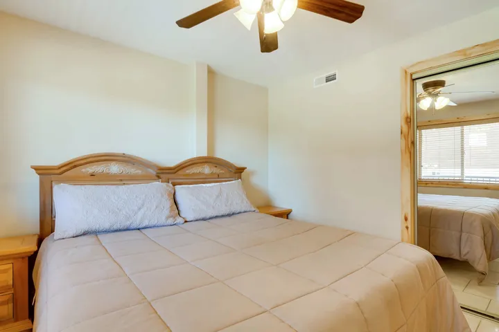Bedroom featuring a ceiling fan with integrated lighting, a mirrored closet door with a natural wood frame, and a window with horizontal blinds