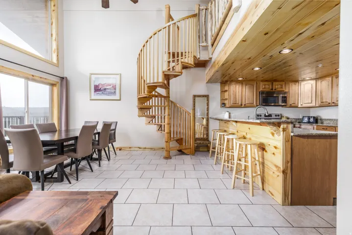 Open-concept living space with a spiral staircase, large windows, tiled flooring, wood-finish kitchen cabinetry, and recessed lighting