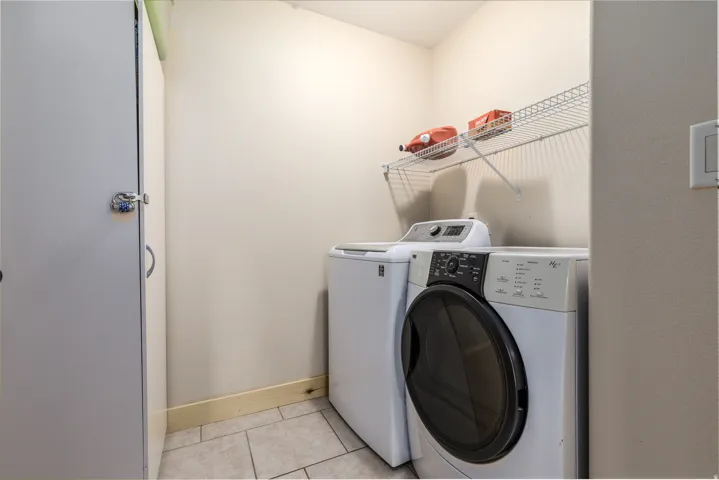 Dedicated laundry area featuring ceramic tile flooring, a built-in wire shelving unit, and a utility cabinet with chrome hardware