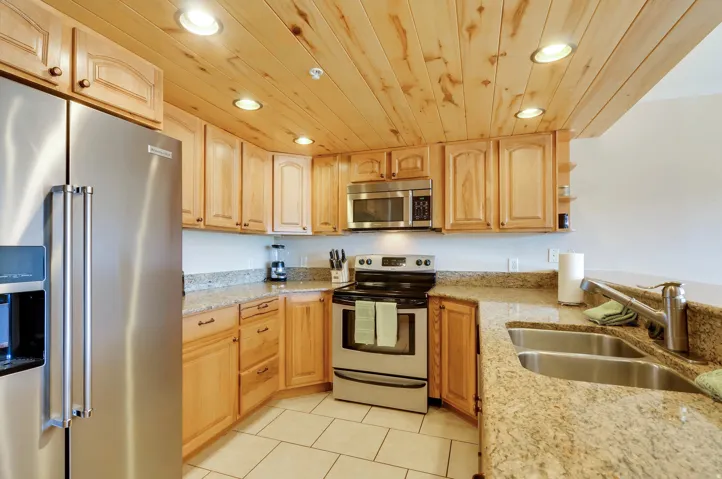 Kitchen featuring wood cabinetry, stainless steel appliances, speckled stone countertops, and a wood-paneled ceiling with recessed lighting