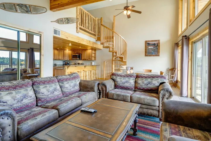Vaulted ceiling great room featuring exposed wood beams, a spiral staircase with log railing, and a full-light sliding glass door