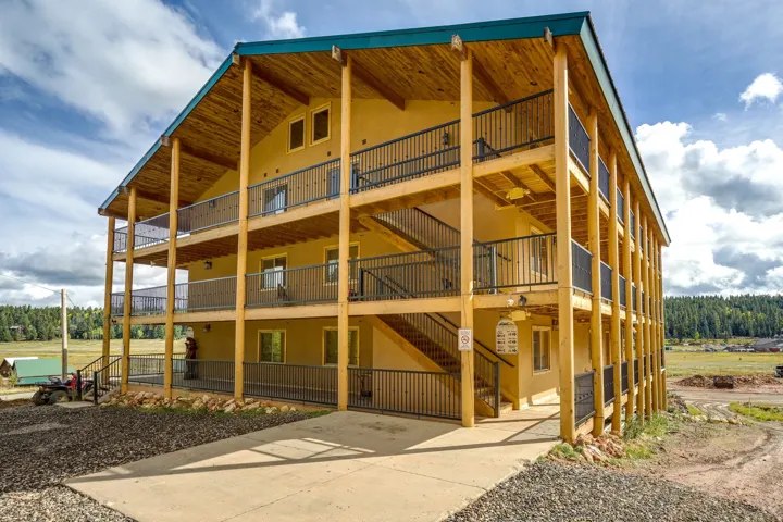 Three-story exterior featuring a turquoise roof, wood-finish columns, stucco siding, multiple balconies with black railings, and a concrete driveway