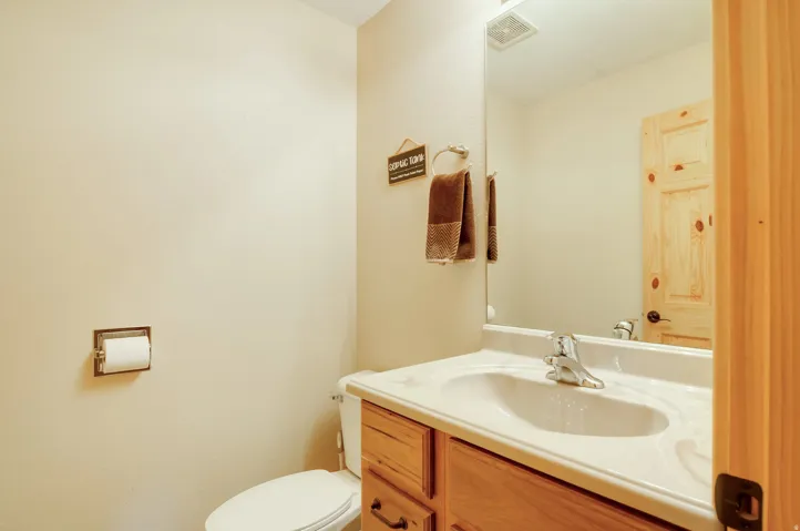 Bathroom featuring a wood-finish vanity with a single basin sink, wall-mounted mirror, and a natural wood-finish door