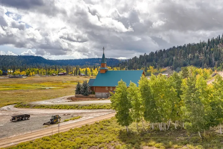 Wood-sided structure with a green metal roof and steeple, situated on a verdant landscape