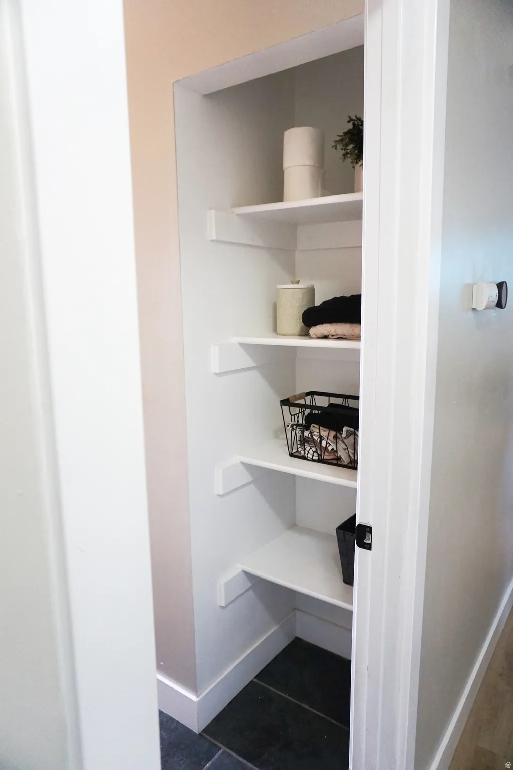 Recessed shelving unit featuring four white shelves, a dark tile floor, and a neutral wall color