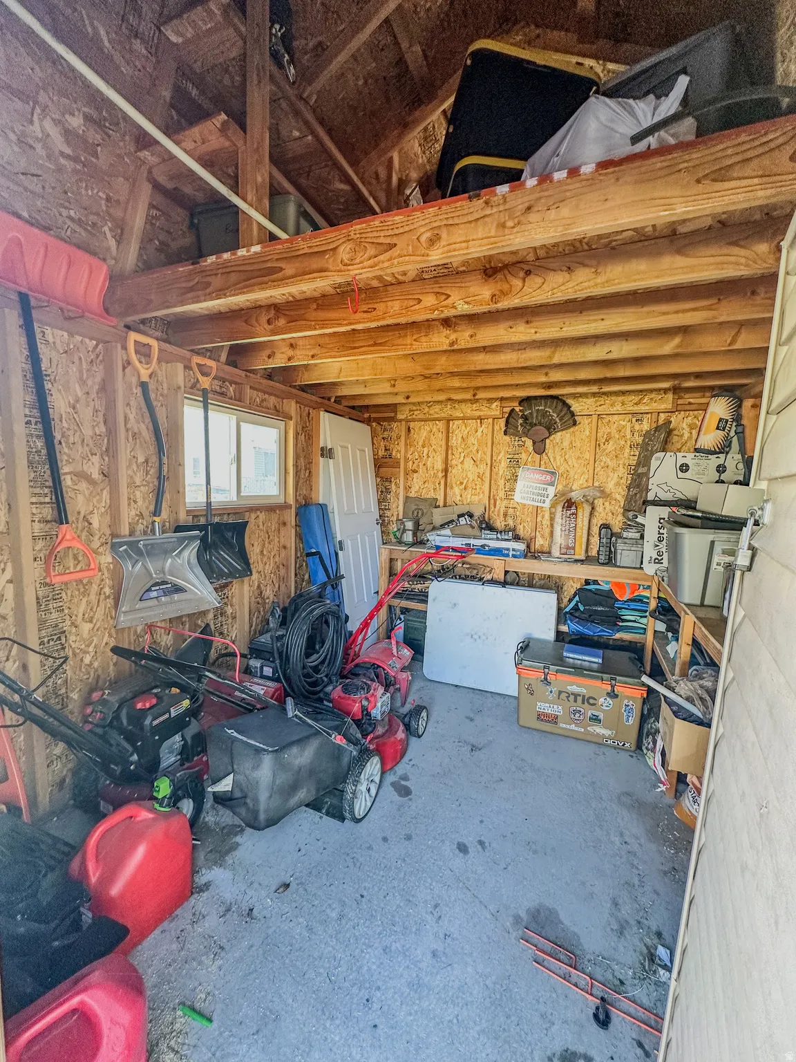 Detached utility shed featuring exposed wood framing, a concrete floor, and an overhead storage loft