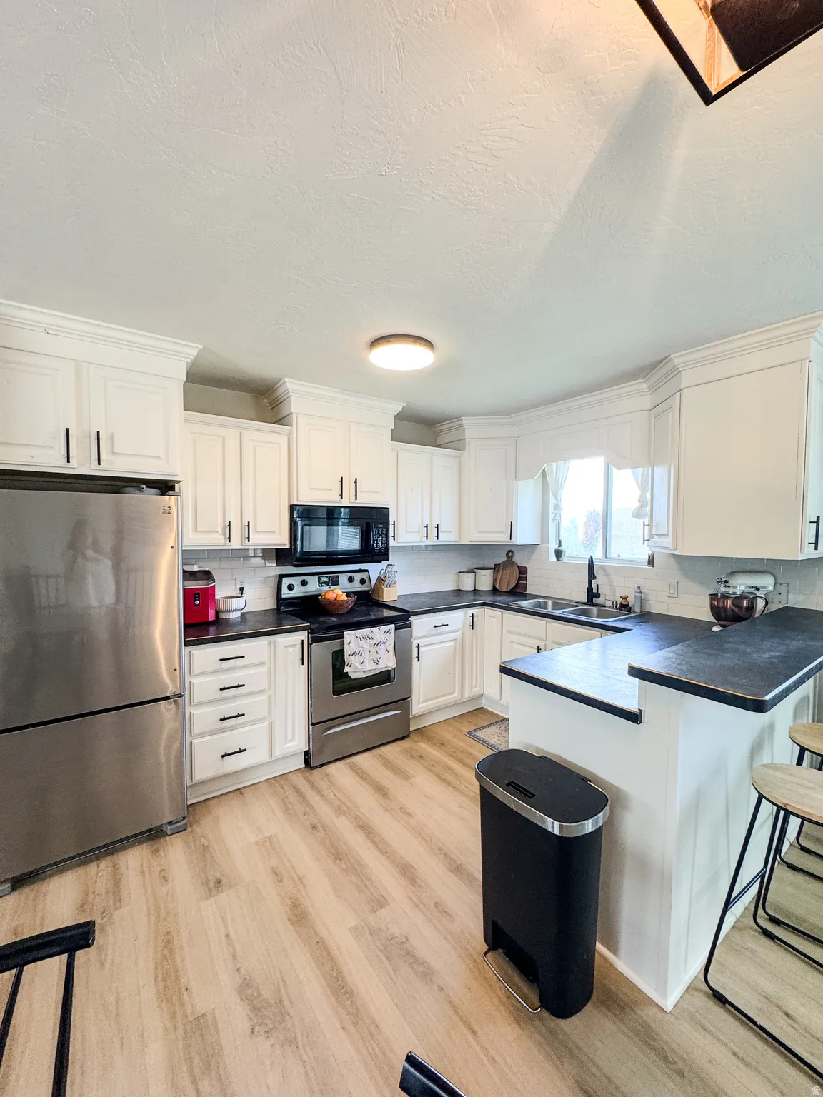 Modern kitchen featuring white cabinetry, stainless steel appliances, dark countertops, wood-finish flooring, and a breakfast bar
