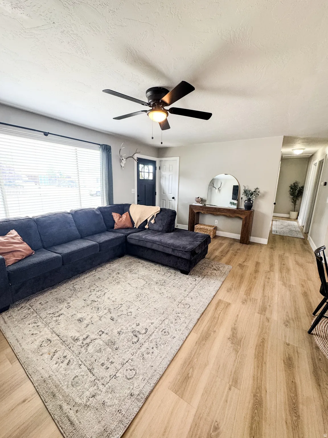 Open concept living space featuring light wood-finish flooring, a contemporary ceiling fan with integrated lighting, and a front entry door with glass paneling
