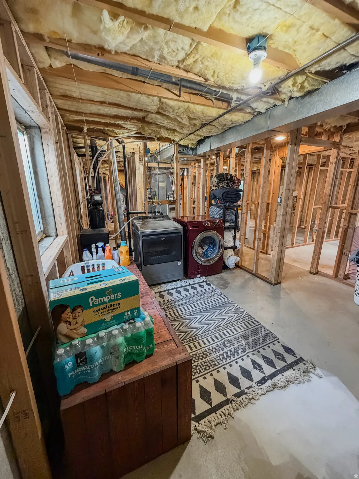 Unfinished basement space featuring exposed wooden framing, visible insulation, and concrete flooring