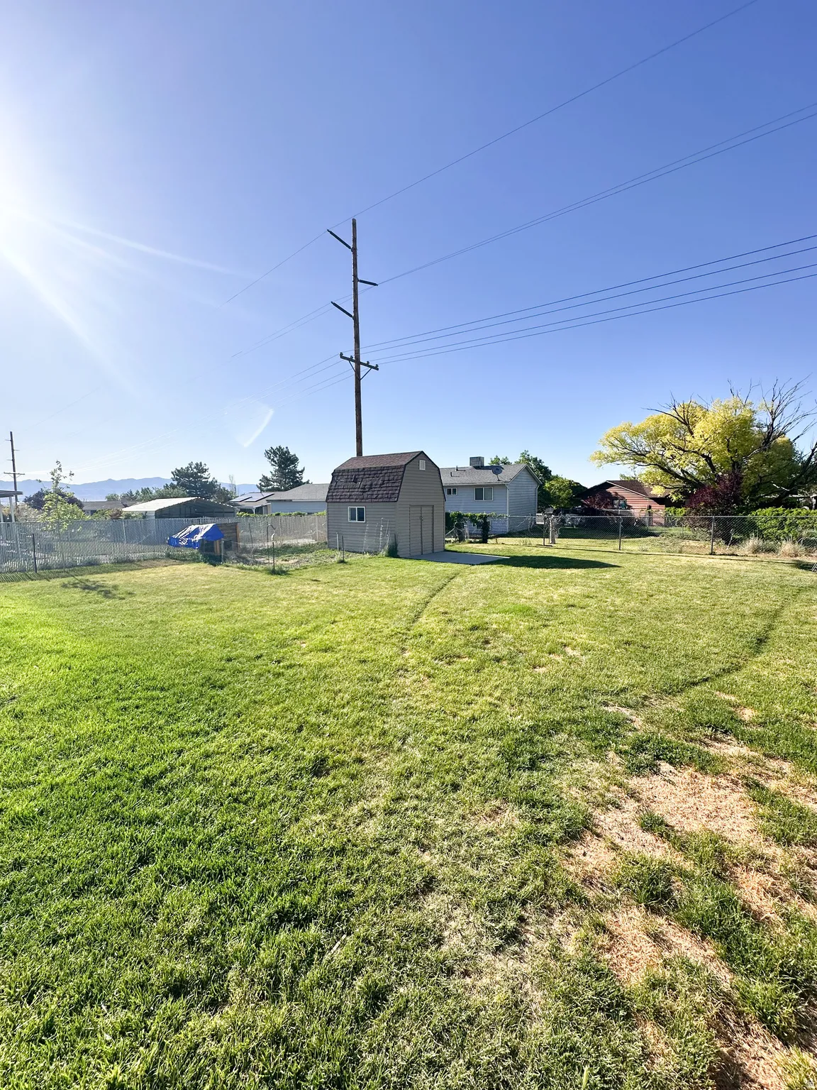 Expansive backyard featuring a storage shed with a shingle roof, a chain-link fence, and a large grassy area
