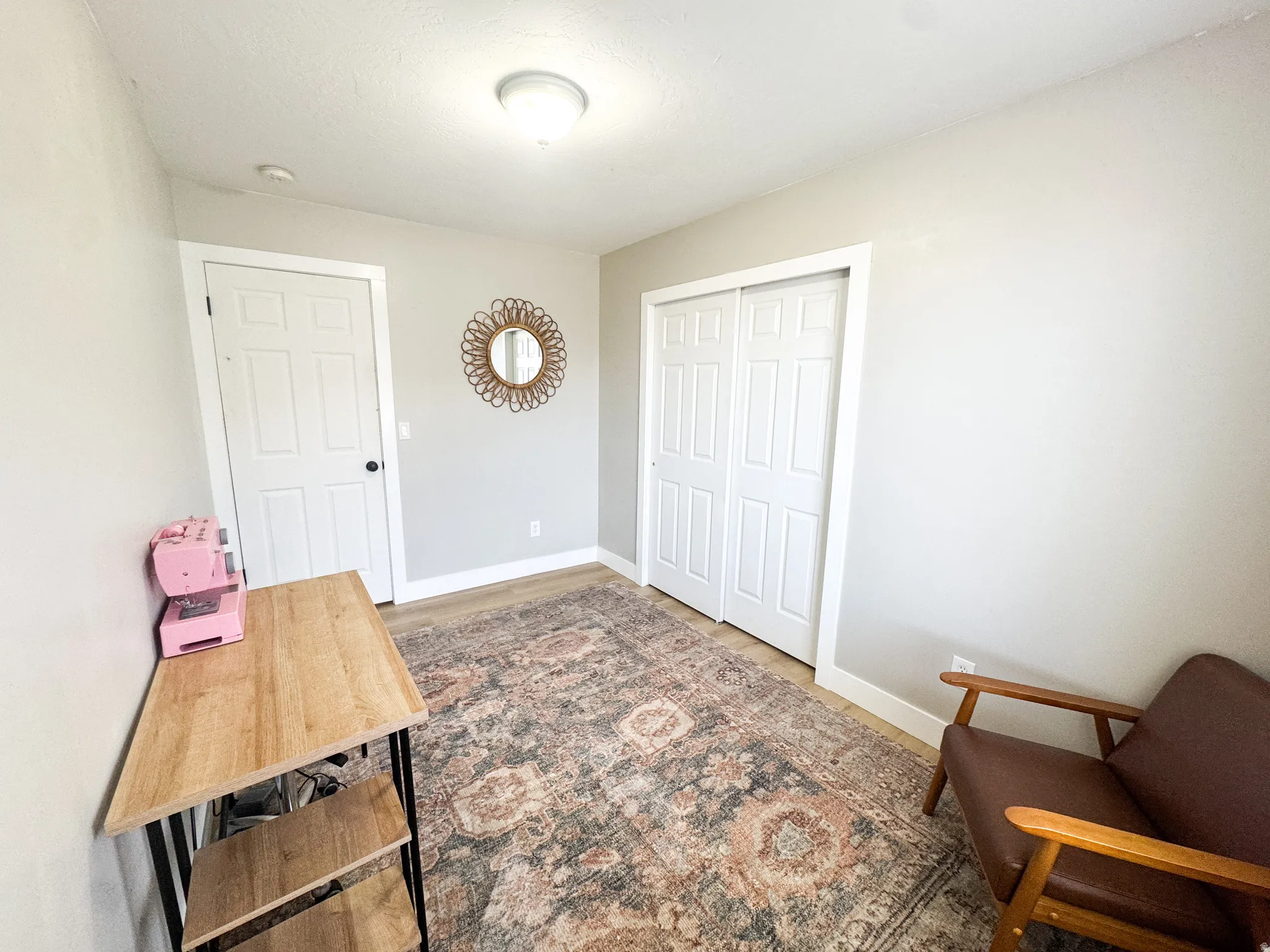 Light-toned walls with contrasting white trim, wood-finish flooring, a white paneled door with black hardware, and a double bi-fold closet door