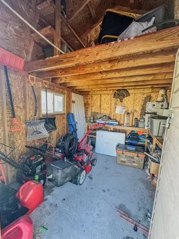 Detached utility shed featuring exposed wood framing, a concrete floor, and an overhead storage loft
