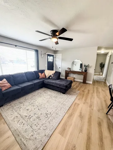 Open concept living space featuring light wood-finish flooring, a contemporary ceiling fan with integrated lighting, and a front entry door with glass paneling