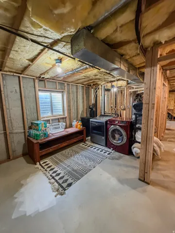 Unfinished basement space featuring exposed wood framing, concrete flooring, and a small window