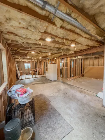Exposed ceiling joists with insulation, bare wall studs, and concrete flooring