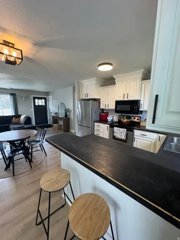 Open-concept kitchen featuring white cabinetry, stainless steel appliances, and dark countertops