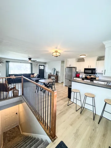 Open-concept living space featuring wood-finish flooring, white cabinetry, a kitchen island with bar seating, a built-in electric range, and a stainless steel refrigerator