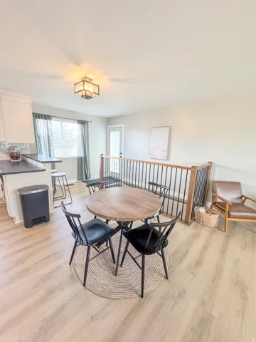 Open-concept living space featuring wood-finish flooring, a contemporary ceiling light fixture, a window with natural light, a white exterior door, and a staircase with a wooden handrail and black metal spindles