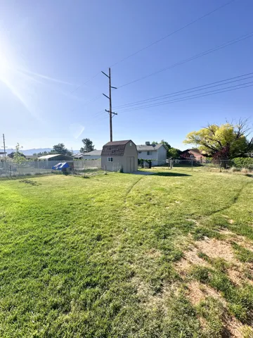 Expansive backyard featuring a storage shed with a shingle roof, a chain-link fence, and a large grassy area