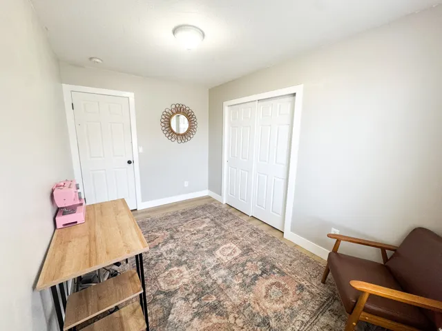 Light-toned walls with contrasting white trim, wood-finish flooring, a white paneled door with black hardware, and a double bi-fold closet door
