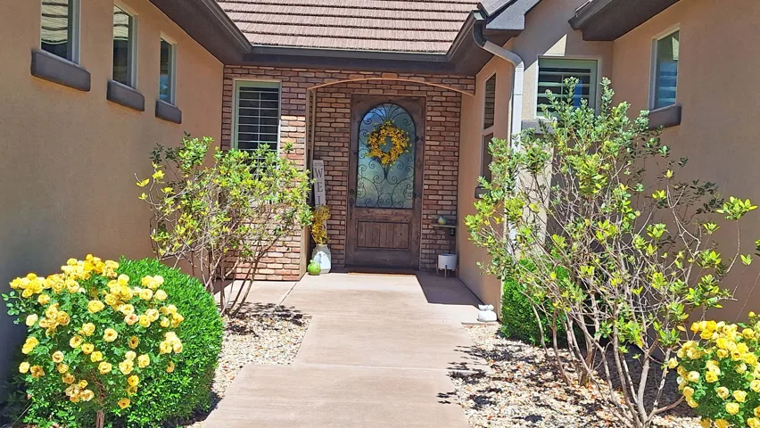 Inviting entryway featuring a wood-finish door with decorative glass, a brick facade accent, stucco exterior, and a concrete pathway