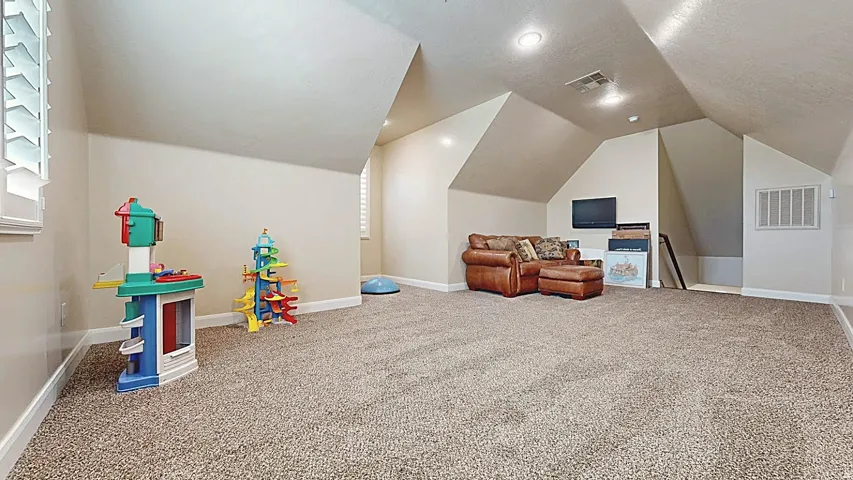 Spacious room with sloped ceilings, recessed lighting, carpet flooring, and window with plantation shutters
