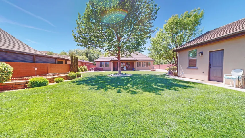 Expansive lawn area featuring a mature shade tree, perimeter planter beds with established shrubs, and a stucco exterior with a tiled roof and 1 bedroom casita