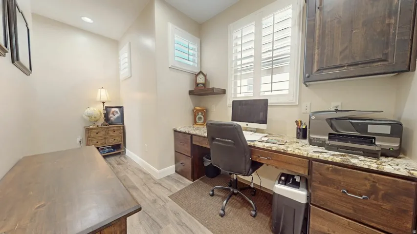 Built-in desk with a stone-finish countertop, wood-finish cabinetry, and plantation shutters