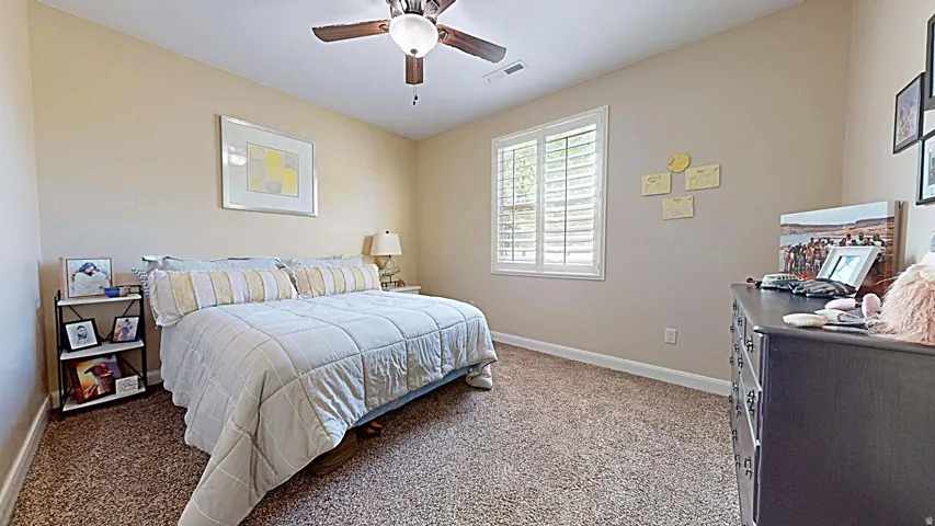 Carpeted room featuring a ceiling fan with light, and a window with plantation shutters