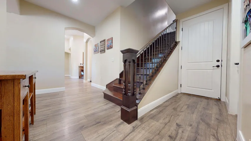 Wood-finish flooring throughout the entry, dark wood staircase with spindle balusters, and arched entryway