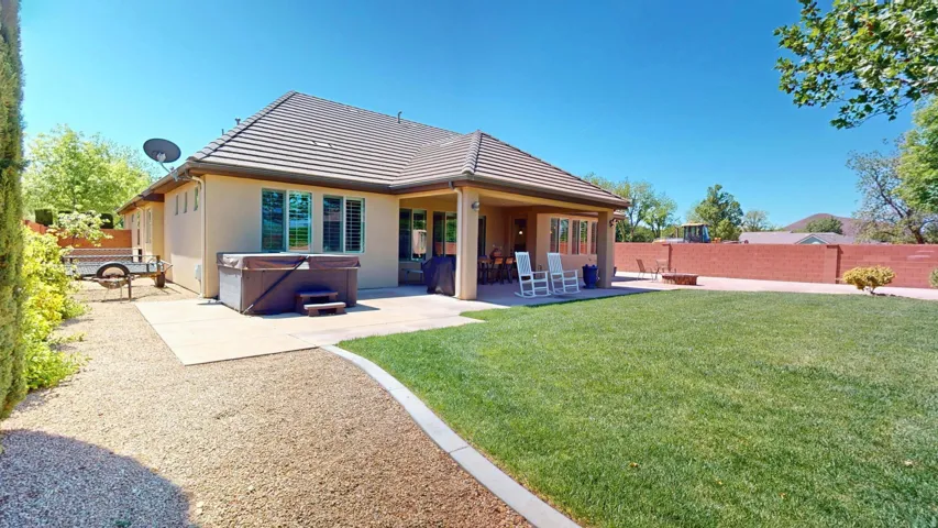 Expansive backyard featuring a manicured lawn, concrete patio, built-in hot tub, and a covered outdoor living area