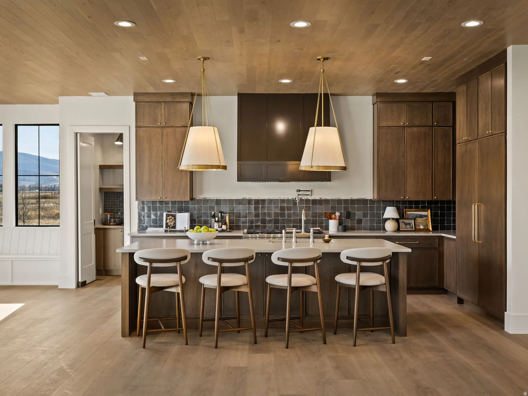 Spacious kitchen featuring a large central island with seating, extensive wood cabinetry, a dark tile backsplash, and wood-finish flooring