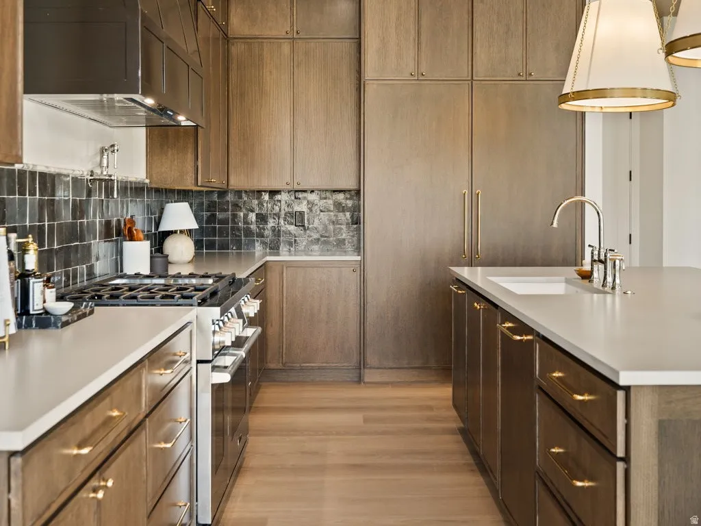 Gourmet kitchen featuring a stainless steel range, custom range hood, wood-finish flooring, recessed lighting, and a kitchen island with an integrated sink and pendant lighting