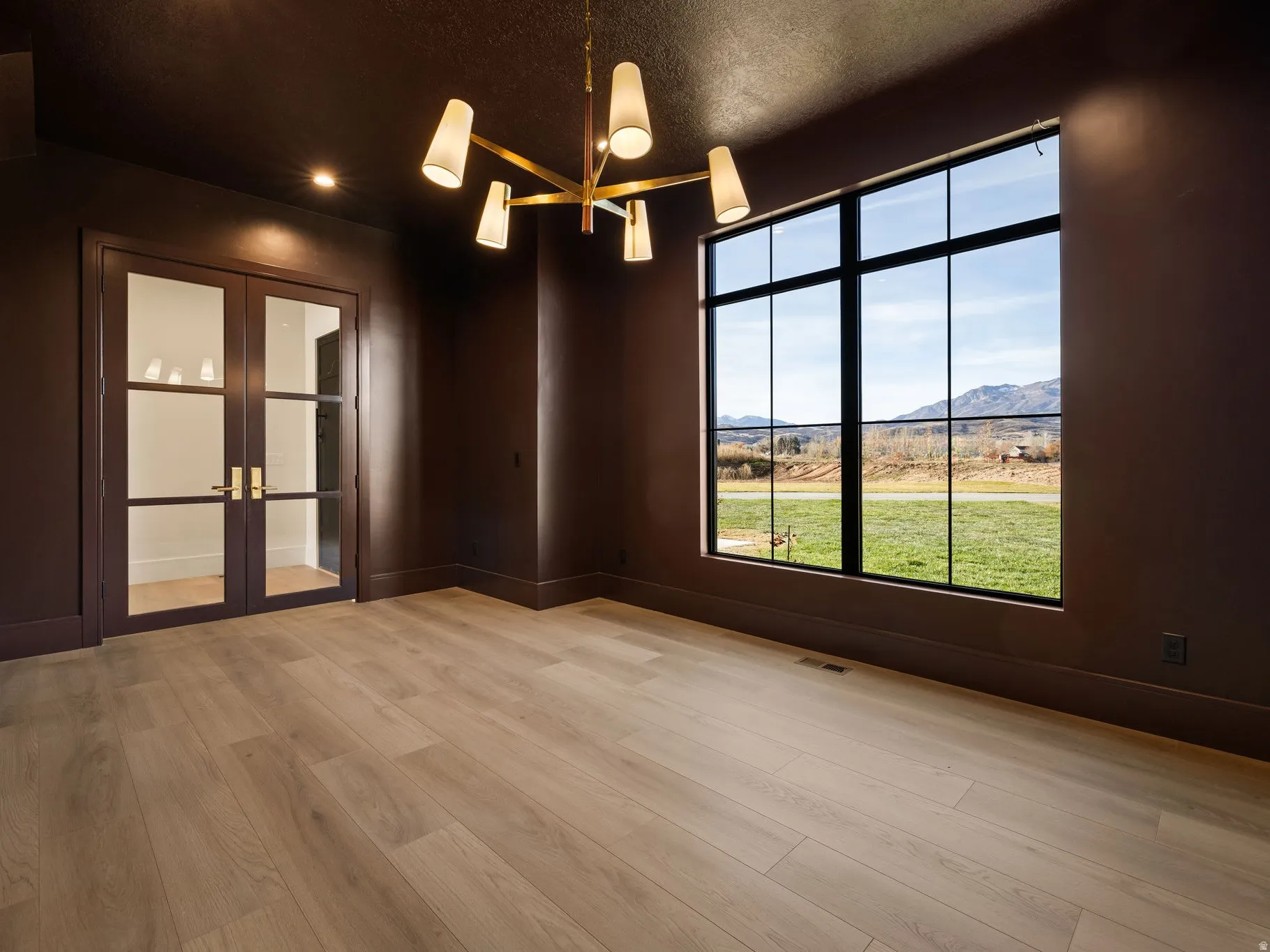 Room featuring a large picture window with mountain scenery, light wood-finish flooring, and dark walls