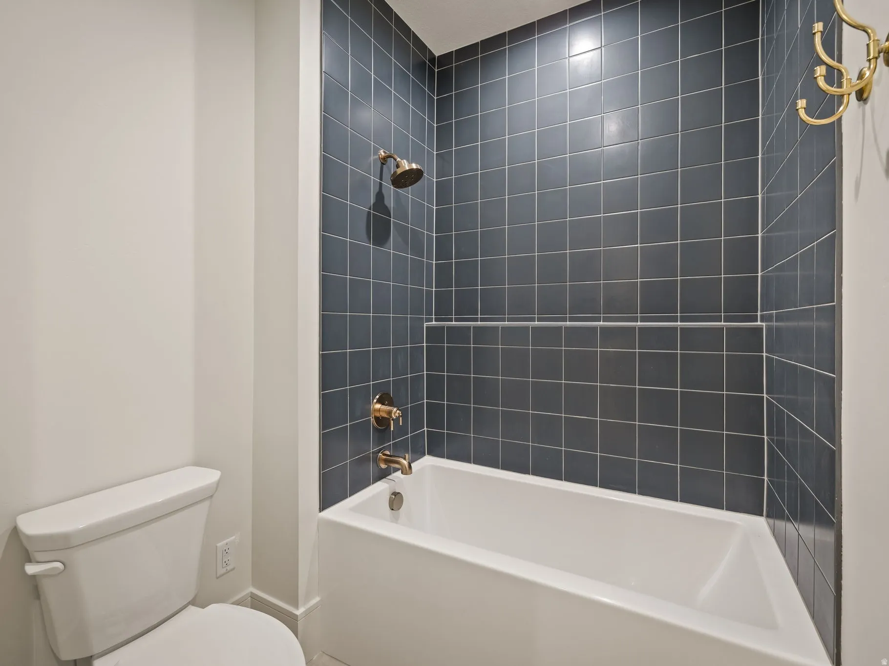 Bathroom featuring a white soaking tub with a dark blue subway tile surround, brass-finish shower fixtures, and a wall-mounted brass-finish coat hook