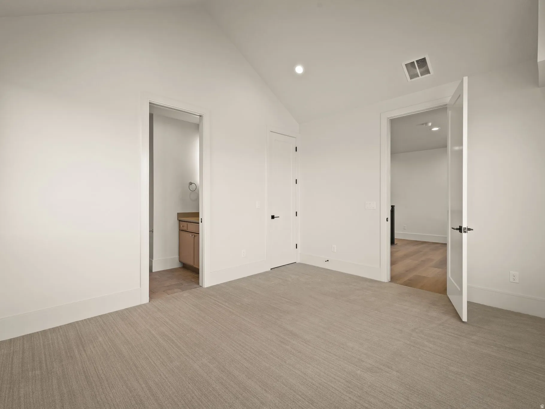 Spacious room featuring vaulted ceilings, recessed lighting, and light-toned patterned carpeting