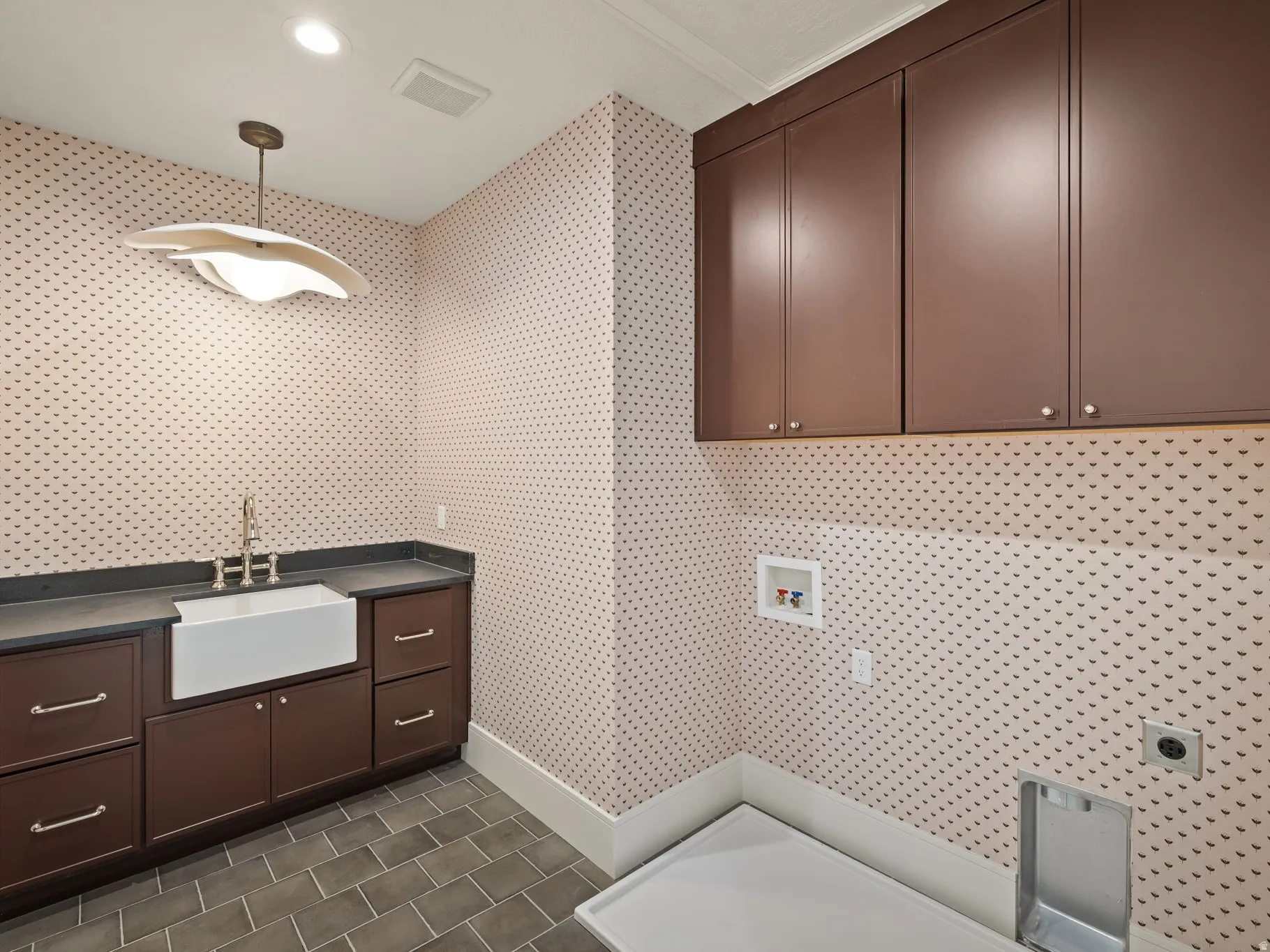 Laundry room featuring built-in cabinetry, a rectangular farmhouse sink with a tall faucet, dark countertops, and tiled flooring