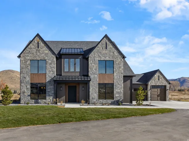 Modern stone and wood-clad exterior with multiple gables, large windows, an attached garage, and a paved driveway