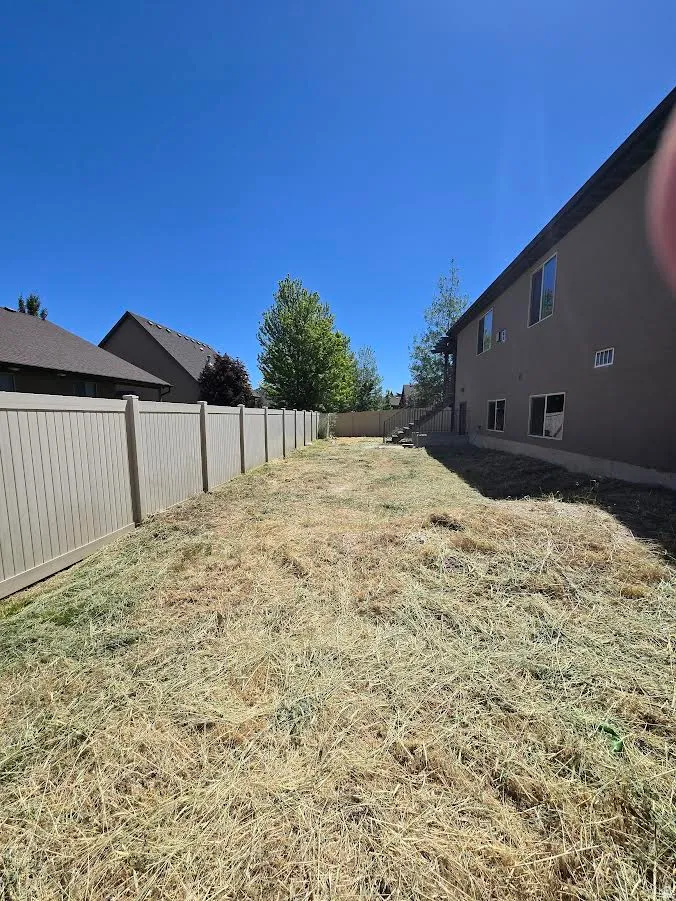 Expansive backyard featuring a light-colored privacy fence and a two-story exterior with multiple windows